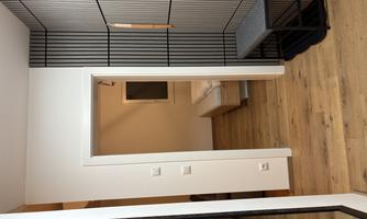 A modern hallway with a mirror and a bench. In the background, a room with a bed and a window is visible.