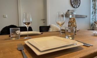 A set dining table with elegant plates and glasses. In the background, a clock and stylish wall decoration can be seen.