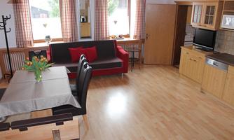 A bright living room with parquet flooring and large windows. There is a dining area with a table, chairs, and a red couch.
