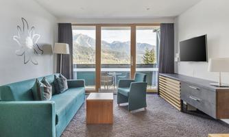 A modern living space with a turquoise sofa and a chair. Large windows offer a view of the mountains.