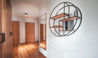 A modern hallway with a wood floor and stylish doors. On the wall is a round mirror with shelves.