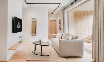 A modern living room with a bright couch, an elegant coffee table, and a large window. The walls are white, and the room has a minimalist style.