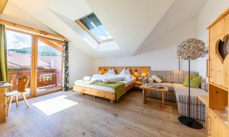 A bright room with a large window and a balcony. There is a double bed, a cozy armchair, and a stylish lamp.