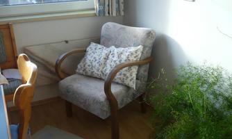 A comfortable armchair with flower-shaped cushions is in a corner of the room. Next to the armchair, there is a green plant and a table.