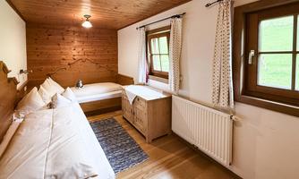 A cozy bedroom with wooden walls and two beds. There is a window with a view and a warm, inviting atmosphere.