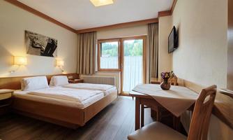 A cozy hotel room with two beds, a table, and chairs. The room has large windows that let in plenty of daylight.