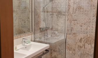 A modern bathroom with a shower cabin and a sink. The walls are lined with patterned tiles.