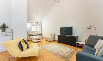 A bright and modern living room with hardwood floors. There is a comfortable sofa, a television, and a cozy armchair.