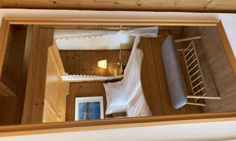 A cozy bedroom with a wooden ceiling and a large bed. The mirror reflects the warm atmosphere and a small table on a wooden floor.