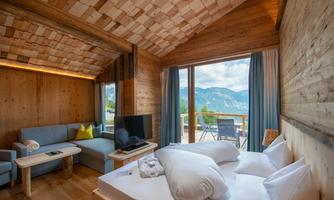 A modern room with wooden decor and large windows. The view includes mountains and a cozy seating area.