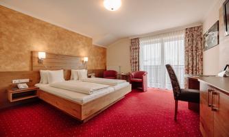 A cozy hotel room with two single beds and a desk.  
Large windows provide plenty of daylight, and there is a pleasant carpet.