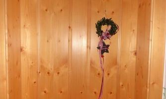 A wooden door with a decorative wreath and a sign above. The door has a natural grain and a simple design.