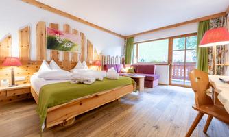 A cozy room with wooden furniture and a beautiful view. The bed is decorated with white pillows and a green blanket.