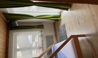 A simple room with a loft bed and a window. The curtains are green and the floor is made of wood.