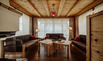 A cozy living space with a wooden ceiling and large windows. Two sofas and a wooden table create an inviting atmosphere.