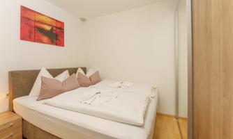 A cozy bedroom with a double bed and decorative pillows. A modern artwork in warm colors is hanging on the wall.