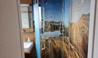 A modern bathroom with a shower cabin and an appealing wall design depicting a natural scene. The wood and tile elements give the room a warm atmosphere.