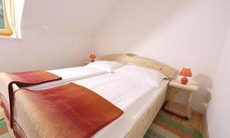 A bright bedroom with two single beds and a wood-colored headboard. Two small lamps are on the nightstand.