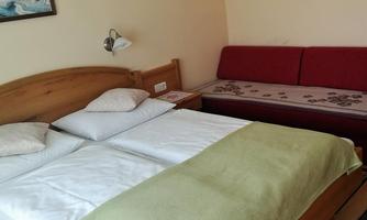 A cozy bedroom with a double bed and a red couch. The walls are in a light shade and there are pictures on the walls.