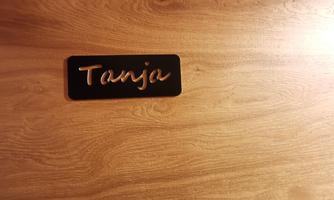 A black nameplate with the inscription "Tanja". It is placed on a wooden surface.