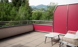 A modern balcony with a table and a chair. In the background, a green landscape and gentle hills can be seen.