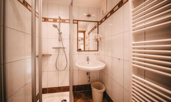 A modern bathroom with a shower and sink. The walls are tiled with light-colored tiles and a heated towel rail is installed.