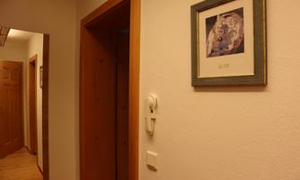 A hallway with a phone and a picture frame on the wall. In the background, an open door is visible.