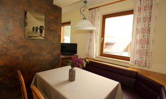 A cozy dining area with a table and a flower vase. The window lets in ample natural light and there are decorative curtains.