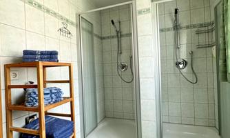 A modern bathroom with two shower cabins.  
Towels and bath mats in fresh colors create an inviting atmosphere.