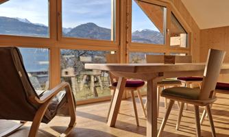 A bright room with wooden paneling and large windows that offer a view of the mountains. A table and chairs are in the room, creating an inviting atmosphere.