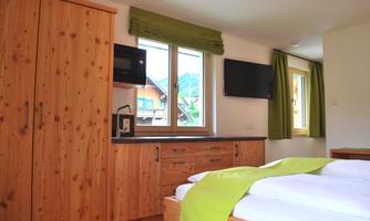 A cozy bedroom with wooden furniture and green curtains. There is a television and a small kitchen area.