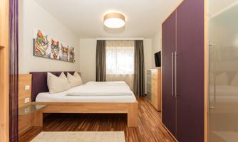 A modern bedroom with two single beds and a large window. On the wall hangs a colorful art print featuring cat motifs.