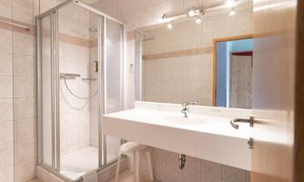 A modern bathroom with a shower and a large sink. The walls are tiled in light colors and there is good lighting.