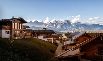 A picturesque mountain landscape with traditional wooden houses. In the background, majestic mountains rise under a clear sky.
