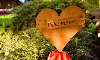A heart-shaped sign with the inscription "Welcome" stands amidst greenery. It radiates an inviting atmosphere.