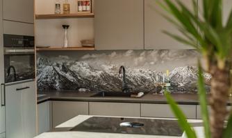 A modern kitchen with wooden shelves and an elegant countertop. In the background, there is a stunning mountain landscape depicted.