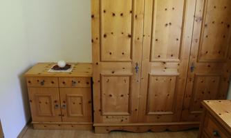 A bright room with pine wood furniture. On the left is a dresser and on the right a large wardrobe.