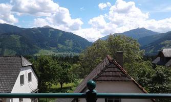 A picturesque mountain landscape with lush forests and gentle hills. The sky is clear and adorned with white clouds.