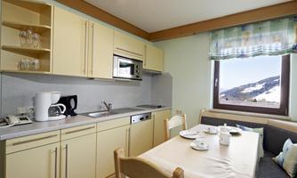 A bright kitchen unit with modern fittings and a dining table. A snow-covered landscape is visible through the window.