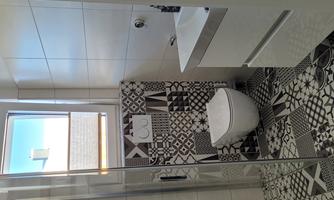 A modern bathroom with a glass shower wall and a stylish sink. The floor is designed with geometric tiles in black and white.