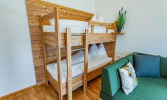 A cozy room with a wooden loft bed and a green sofa. The walls are light and there is a plant for decoration.