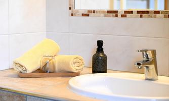A modern bathroom with a sink and a faucet. There are fresh, yellow towels and a soap dispenser bottle on the shelf.
