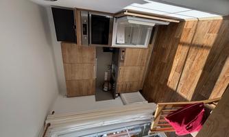 A modern kitchen with wooden cabinets and modern appliances. The room has large windows that let in plenty of daylight.