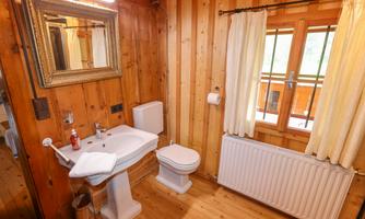 A cozy bathroom with wooden paneling. It contains a sink, a toilet, and a window with curtains.