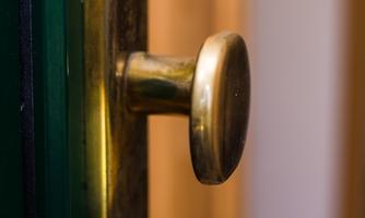 A shiny brass doorknob on a wood surface. The background is blurred, which puts the focus on the doorknob.