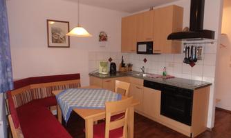 A cozy kitchen with a dining table and a seating area. The furniture is made of wood and the walls are painted in light colors.