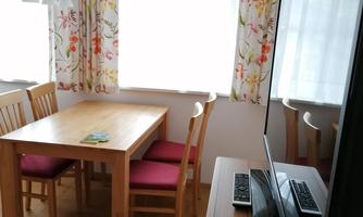 A cozy dining area with a wooden table and chairs. Generous windows provide plenty of daylight, and the TV is next to the table.
