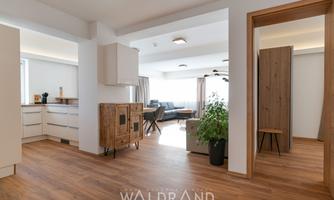 A modern apartment with wooden floors and large windows. The decor is bright and minimalist, featuring a stylish wardrobe and a seating area.