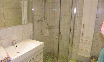 A modern bathroom with a glass shower enclosure. There is a sink with storage and bright tiles on the walls.