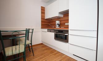 A modern kitchen with white cabinets and wood paneling. A table with chairs sits in the corner.